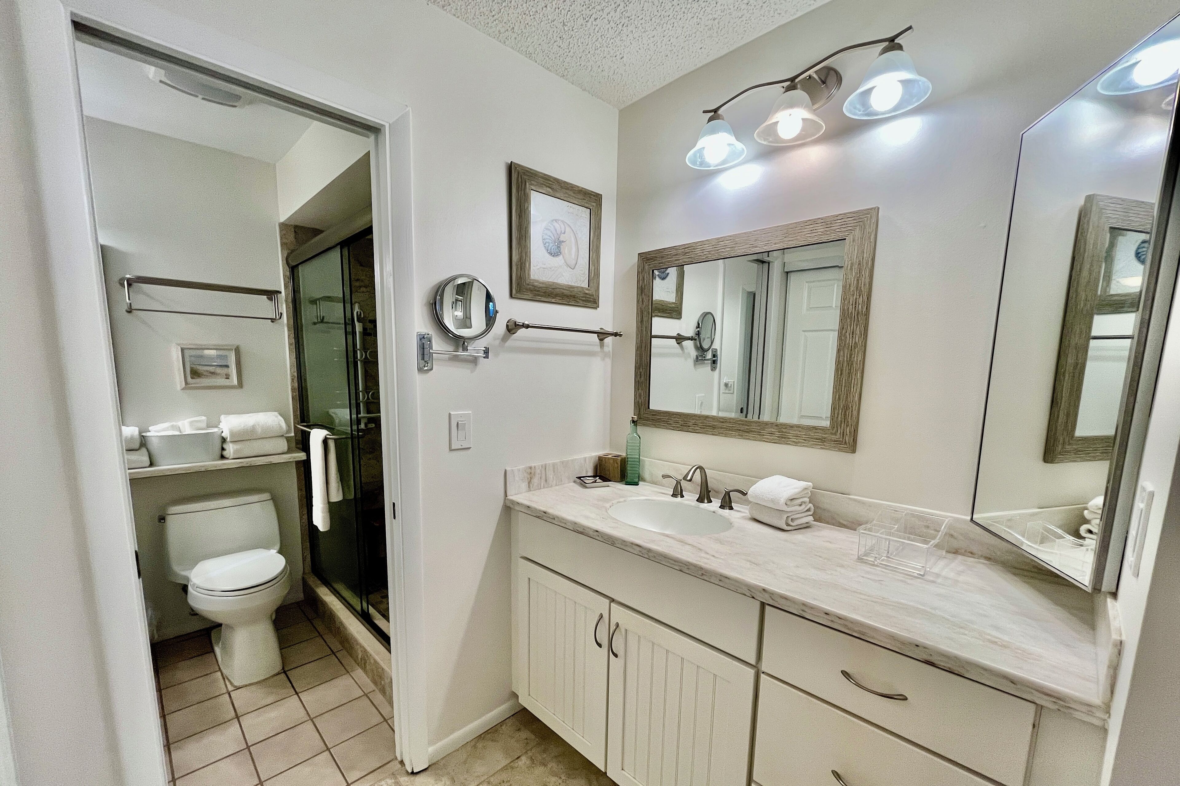 Un baño con inodoro blanco, lavamanos con espejo y zona de ducha.