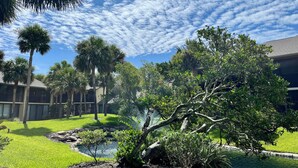 A landscaped garden with a pond, palm trees, and a building with a flat roof. - Best Address at the Beach, Gold-rated condo just a short walk to the beach! (Saint Augustine)