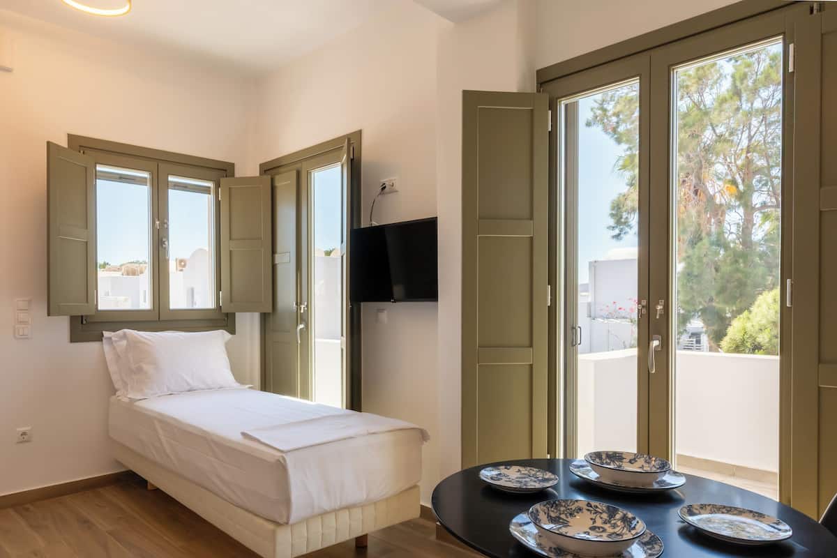 A bedroom with a bed, a table with plates, and a TV on the wall.