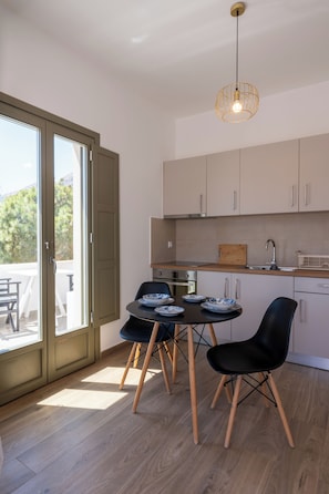 A modern kitchen with a dining area, featuring a sliding glass door to the outdoors, a central island, and a pendant light. - Apeiron Perissa – Apeiron Hotels (Perissa)
