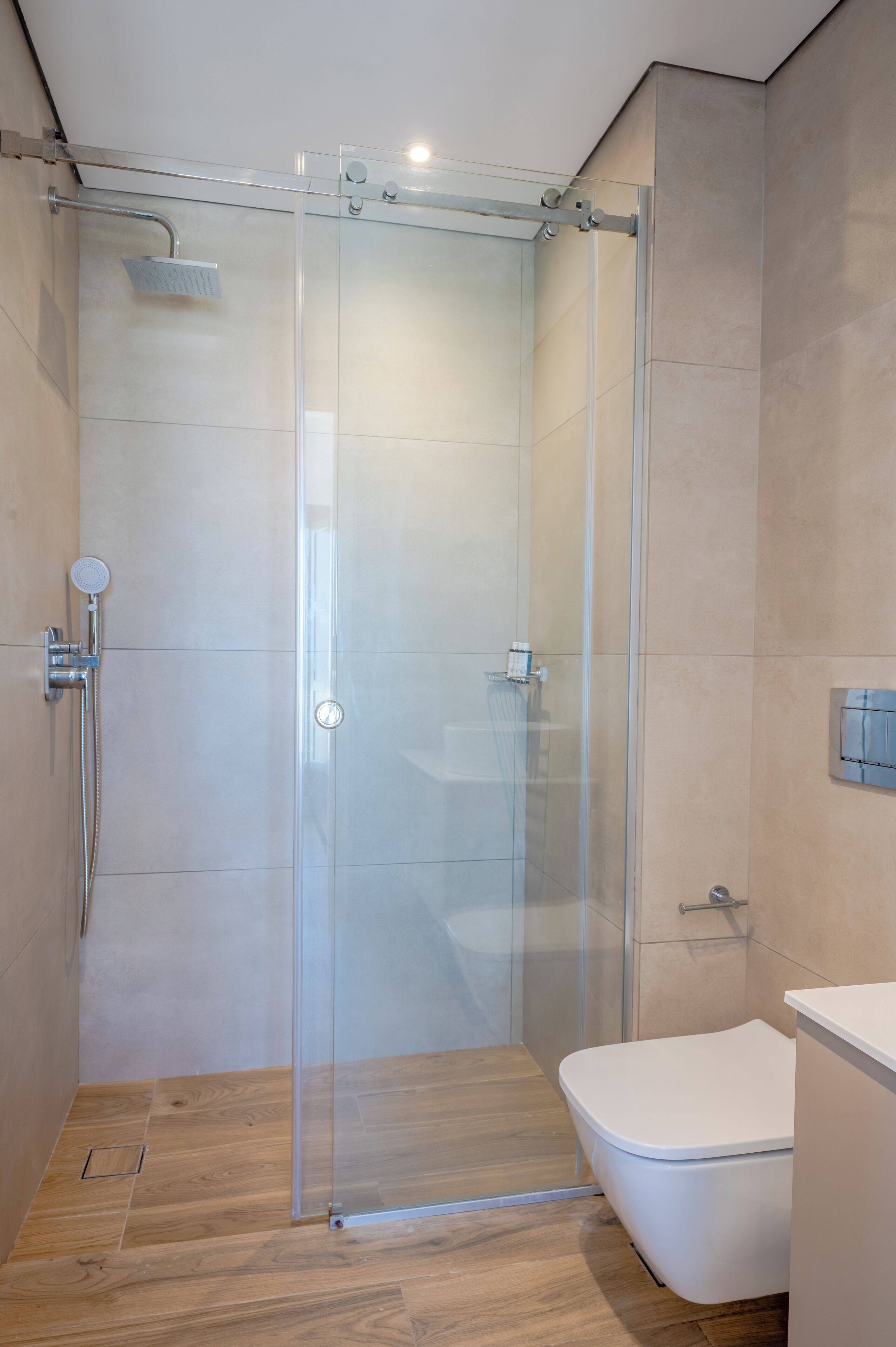 A modern bathroom with a glass-enclosed shower, a white toilet, and a wooden floor.