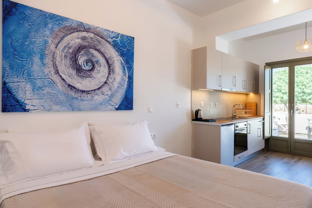 A bedroom with a bed, a kitchenette, and a large abstract painting on the wall.