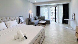 A modern hotel room with a large bed, a sofa, a small table, and a view of the city through large windows. - Gold Coast Mall Nha Trang - LT housing (Nha Trang)