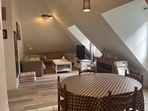 A cozy loft-style living space with a high ceiling, a round dining table, a sofa, a TV, and a star decoration on a cabinet.