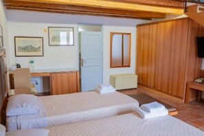 Une chambre d’hôtel avec deux lits, un bureau, une chaise, une armoire en bois et un petit banc.