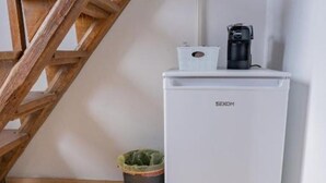 Ett vitt GEKOM-kylskåp med en kaffebryggare ovanpå, en papperskorg och en trätrappa.