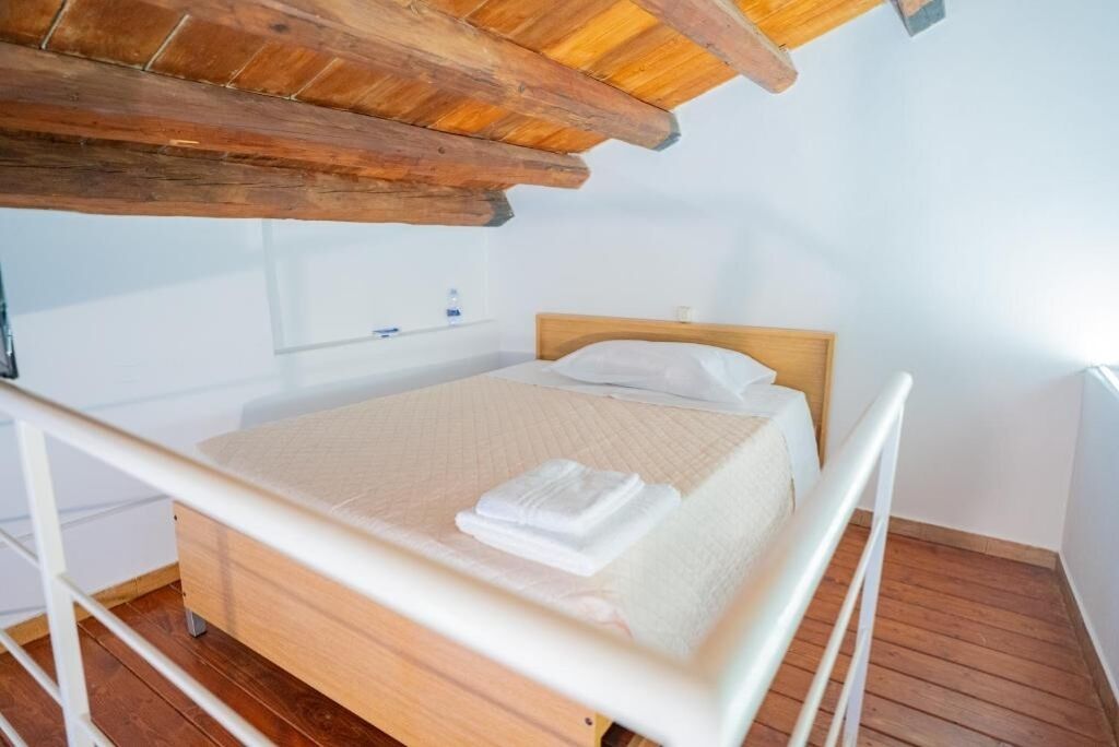 Ein Einzelbett mit hölzernem Kopfteil in einem Raum mit schrägen Wänden und Holzdielen.