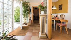 A hallway with a dining area, large windows, and potted plants.