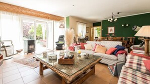 A living room with a glass coffee table, a sofa, and a chair. There is a fireplace, a lamp, and a window with curtains.
