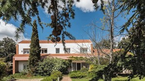 A two-story house with a red-tiled roof, surrounded by a well-maintained garden and trees.