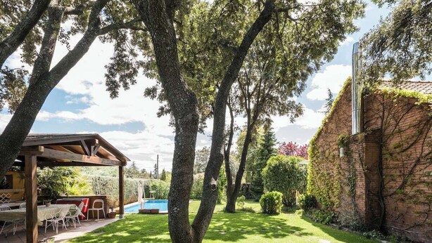 A covered patio with outdoor furniture, a swimming pool, and a brick wall with climbing plants.