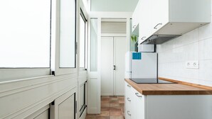 Une cuisine étroite avec des meubles blancs, un plan de travail en bois et un sol carrelé.
