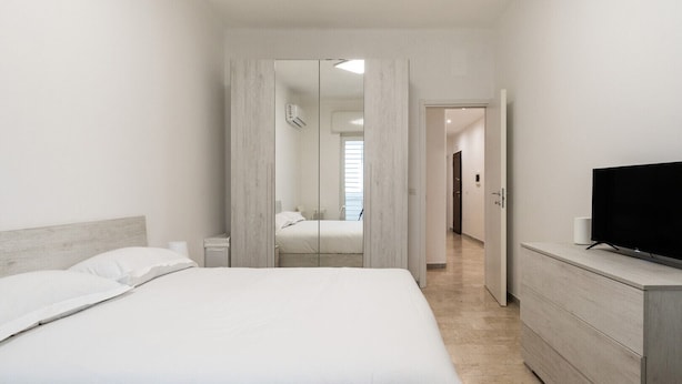 Une chambre d’hôtel moderne avec un grand lit, un téléviseur posé sur une commode et un miroir qui reflète la pièce.