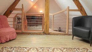 Un dormitori tipus loft amb sostre inclinat, escala de fusta, escriptori, cadira i una alfàbrega amb disseny.