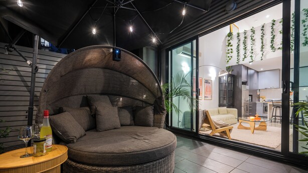 Una sala de estar moderna con un sofá circular, una mesita de madera y un ventanal de vidrio que da a una zona de cocina.