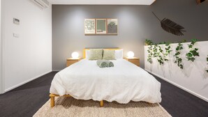 Un dormitorio con cama, lámparas de noche, aire acondicionado instalado en la pared y un adorno mural.