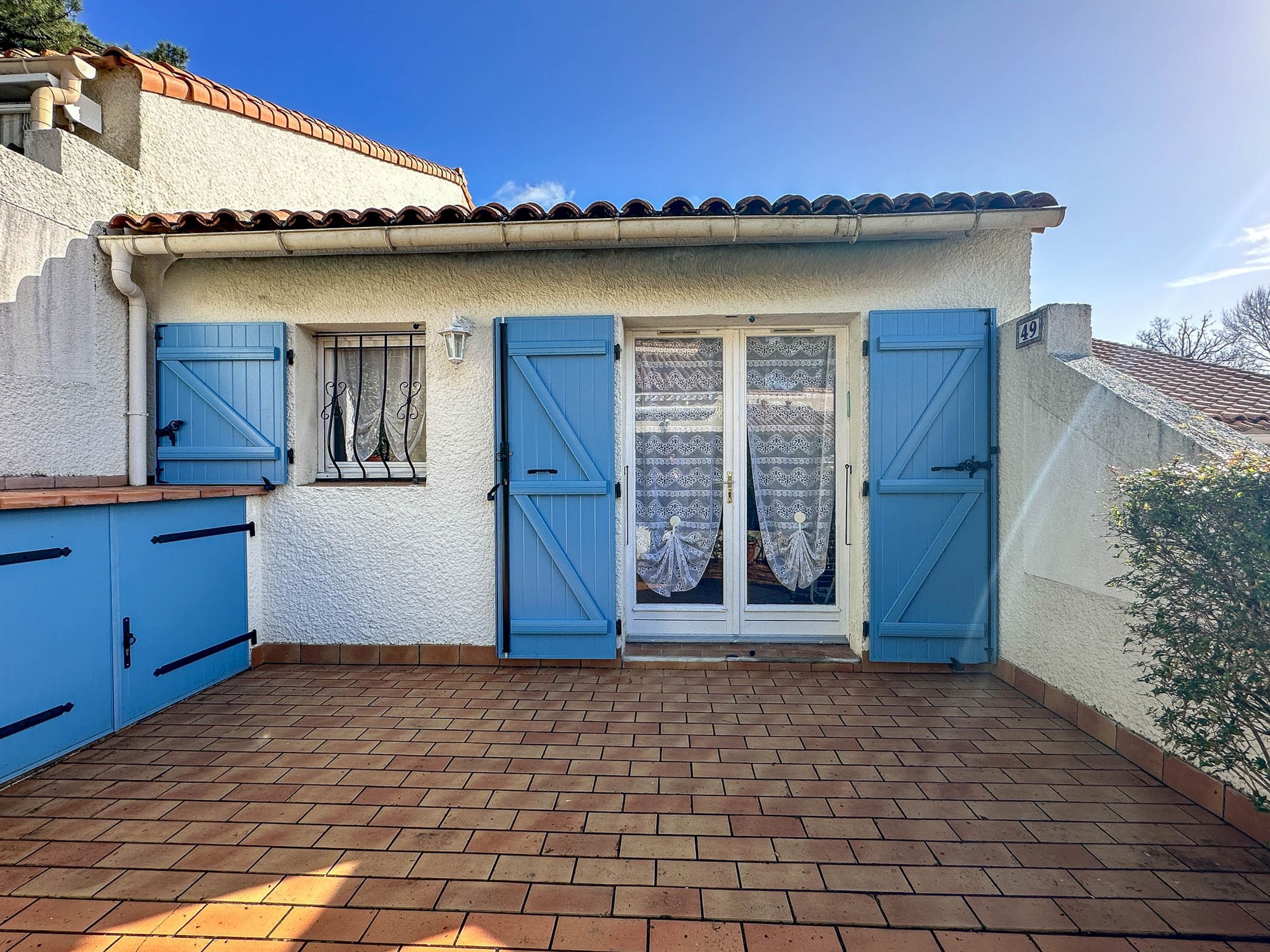 Ein Gebäude mit einem Ziegeldach, einer blauen Tür und einer Ziegelterrasse.