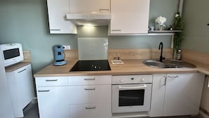 Eine kleine Küche mit weißen Schränken, einem eingebauten Ofen, einer Kaffeemaschine und einem Spülbecken.
