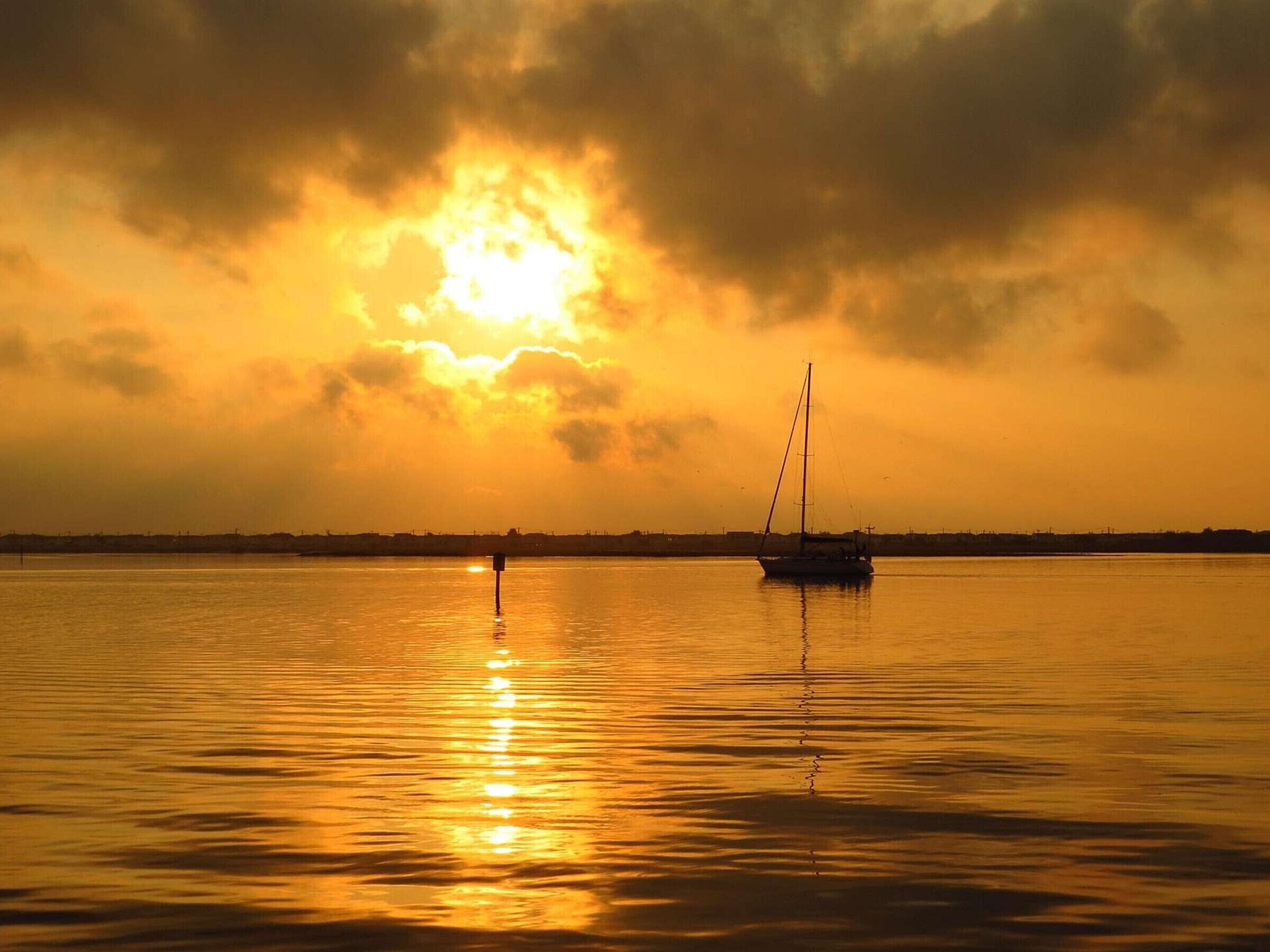 A calm body of water with a sailboat and a distant shoreline.