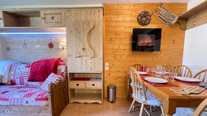 A cozy room with a wooden wall, a fireplace, a dining area with chairs and a table set for two, and a bed with a red blanket. - 2-bedroom apartment at the ski slopes with indoor pool (Flumet)