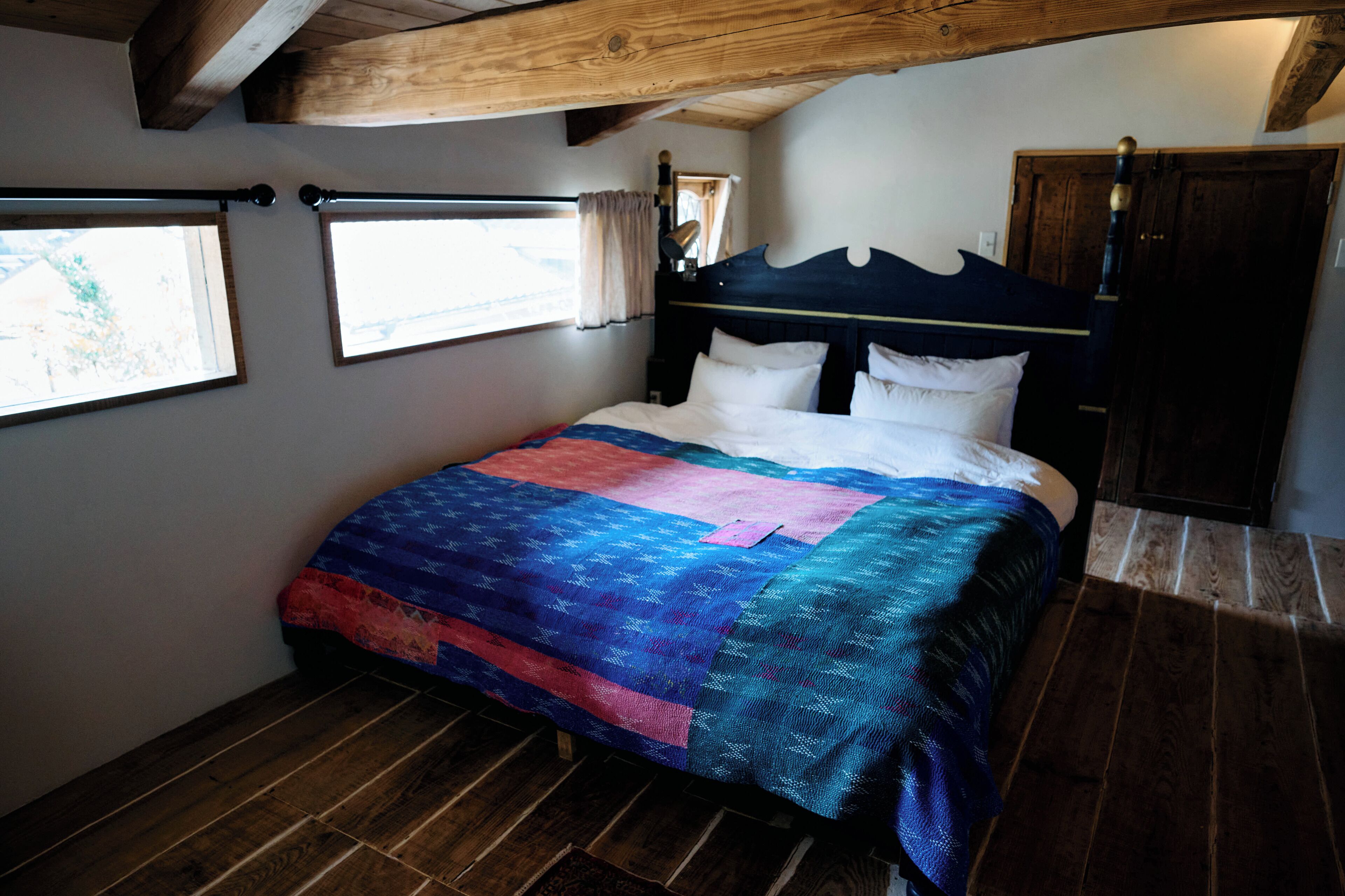 Ein Schlafzimmer mit Holzbalkendecke, einem Bett mit Quiltdecke, einem Fenster und einer Tür.