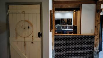 A wooden door with a dreamcatcher, a brick wall, and a glimpse of a kitchen area.