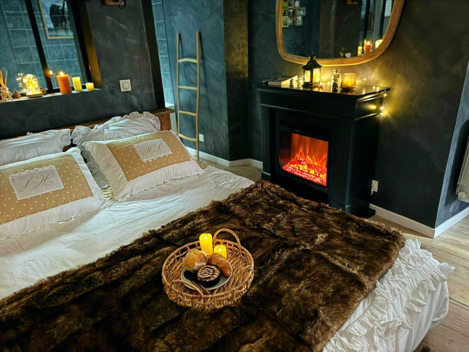 Un dormitorio con cama, chimenea, espejo y una cesta con velas.