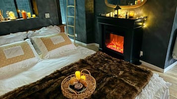 Un dormitorio con cama, chimenea, espejo y una cesta con velas.