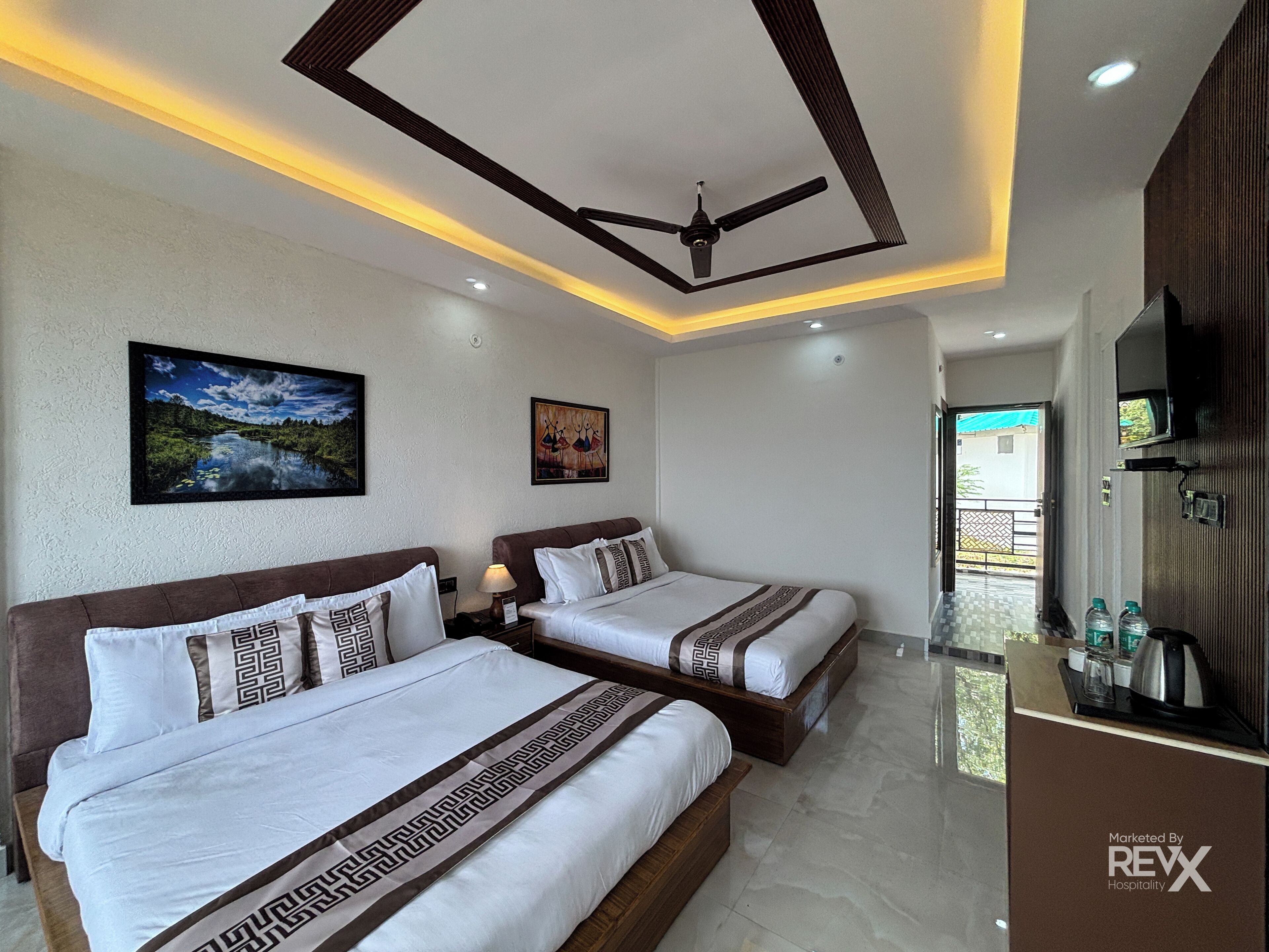 A hotel room with two beds, a ceiling fan, recessed lighting, artwork on the walls, and a minibar.