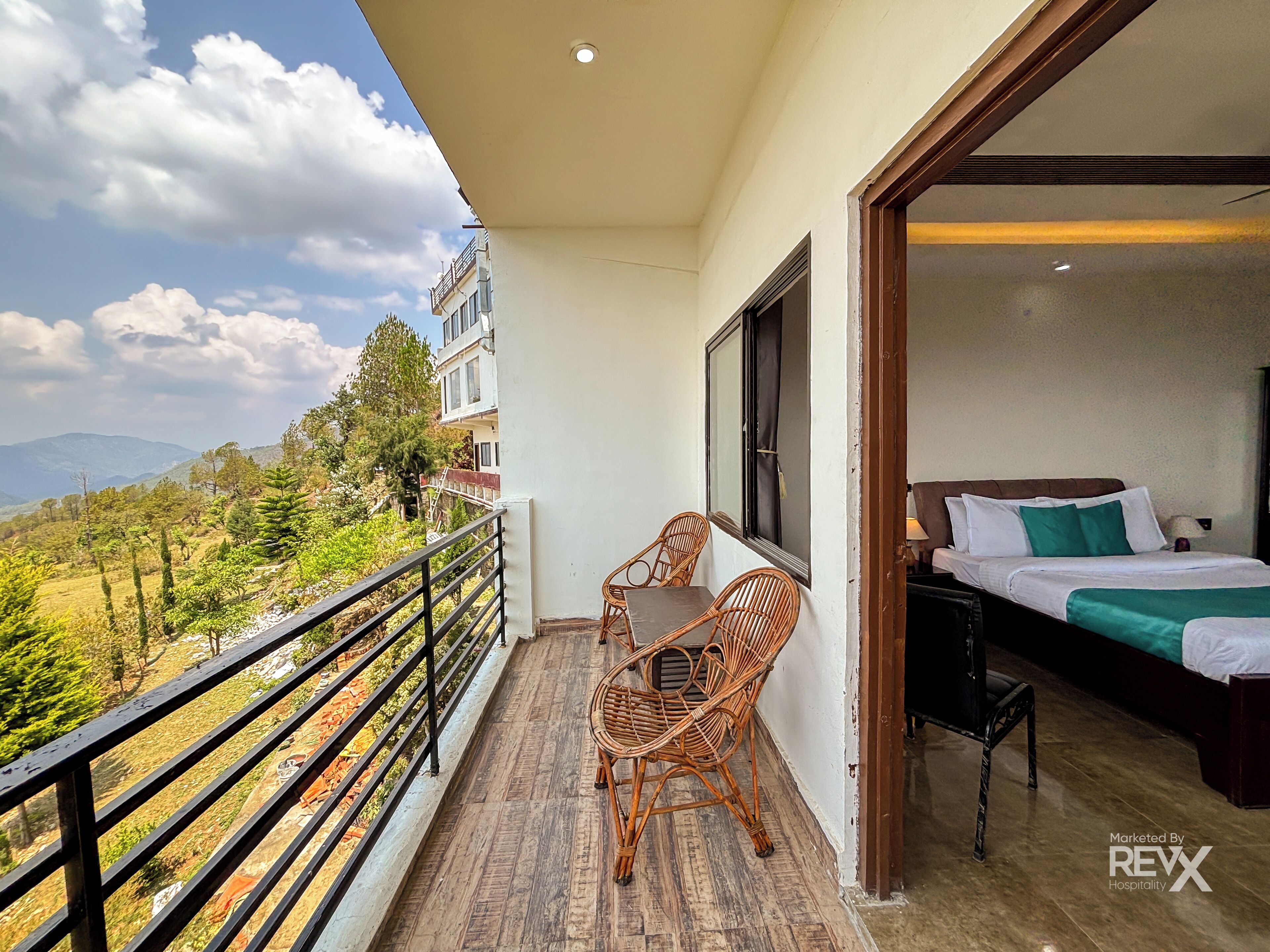 Ein Balkon mit Blick auf eine gebirgige Landschaft, ein Korbsessel und ein Bett mit einem grünen Kissen.