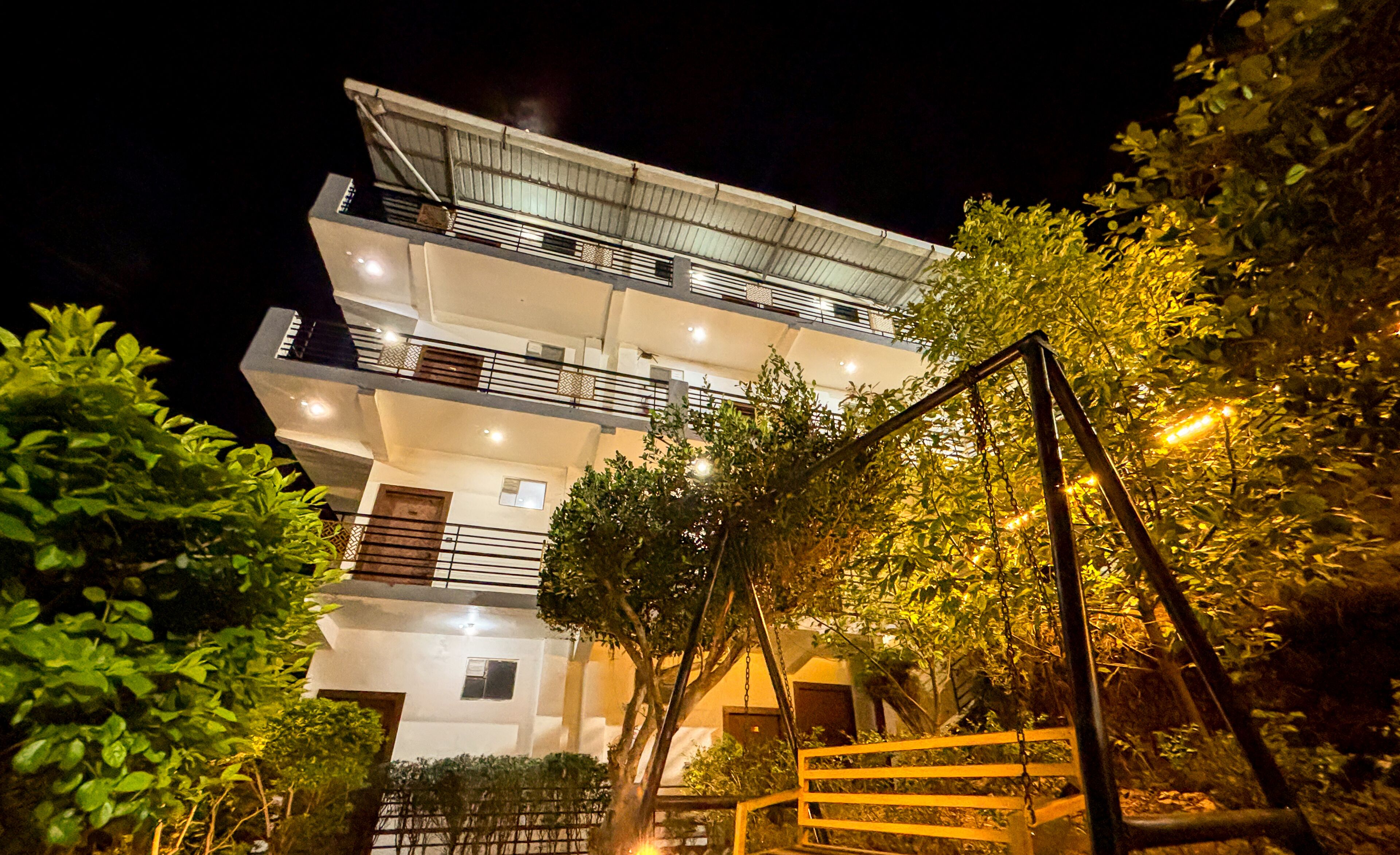 Un edificio de varios pisos con balcones, rodeado de vegetación.