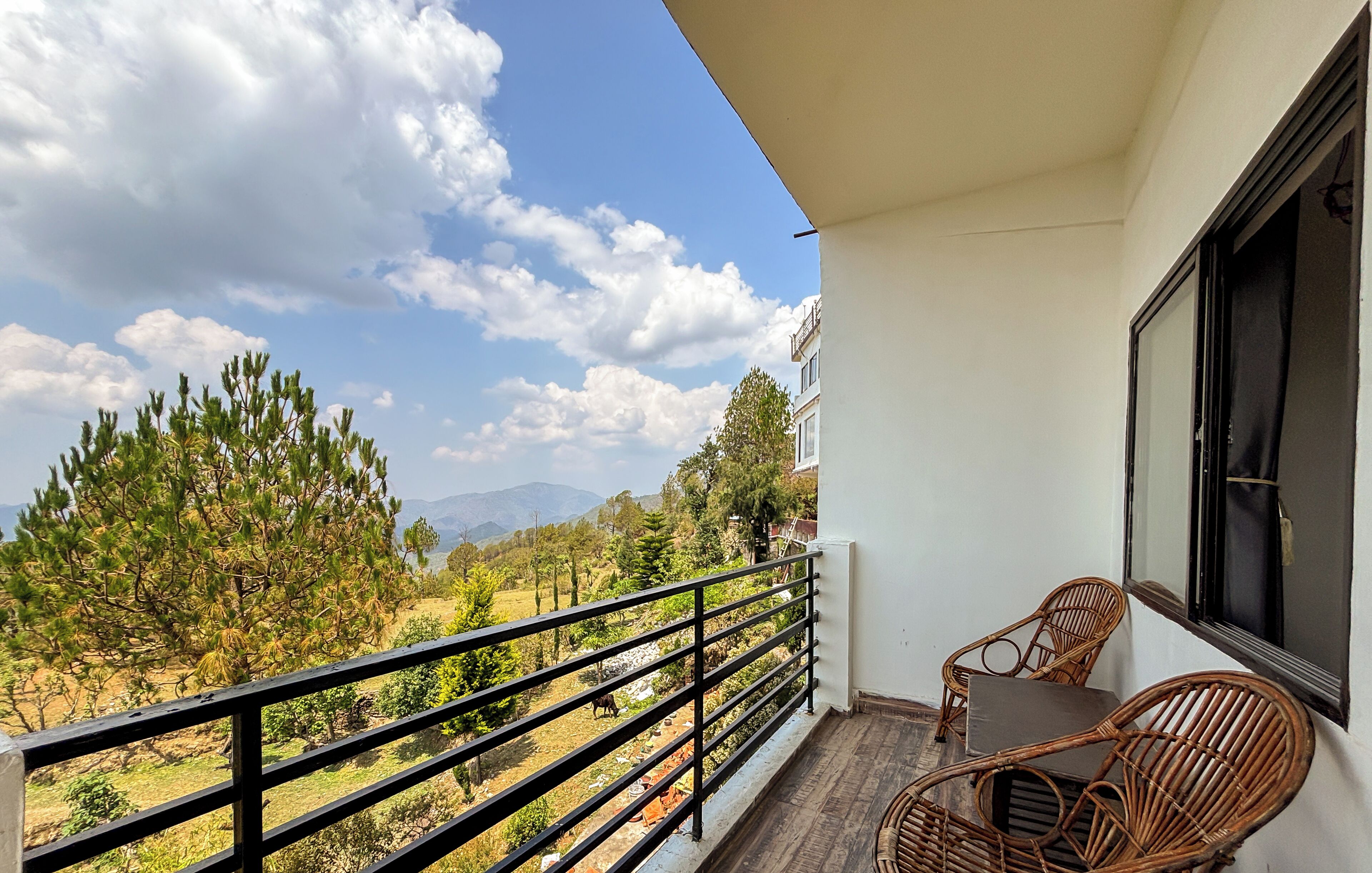 A balcony with wicker furniture, a view of trees and mountains, and a clear sky.