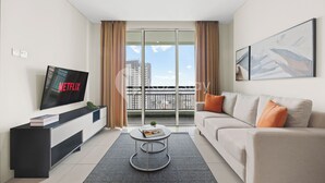 Een moderne woonkamer met een flatscreen televisie, een bank, een salontafel en een balkon met gordijnen.