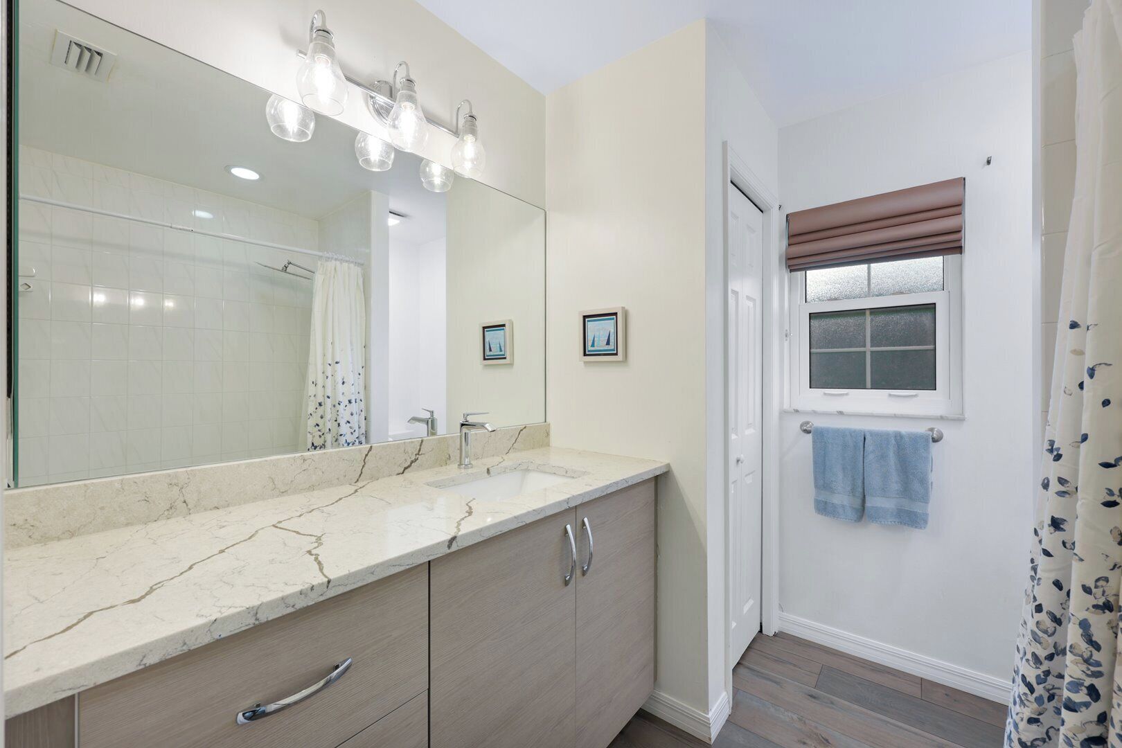 A bathroom with a marble sink, a large mirror, and a window with a brown blind.