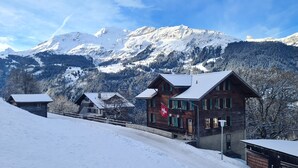 Una cabaña de madera con una bandera suiza, con montañas nevadas y cielos despejados como fondo.