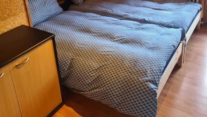 Un dormitorio acogedor y pequeño en el ático, con dos camas individuales, un armario de madera, un radiador y una ventana con cortinas.