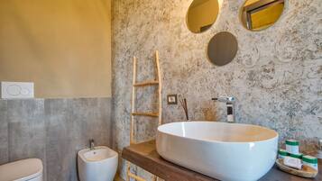 Ein Badezimmer mit einem großen weißen Waschbecken, einer Holzleiter, einem Bidet und einer Marmorwand mit dekorativen Spiegeln.