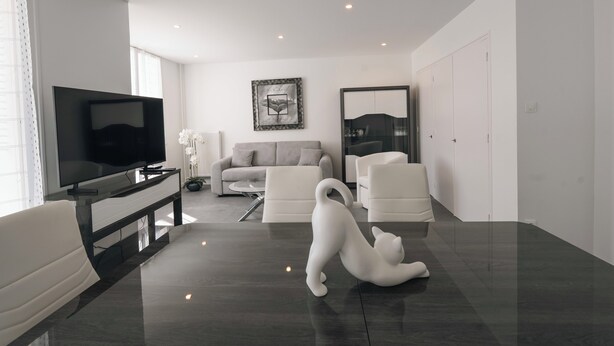 A modern living room with a flat-screen TV, a sofa, two chairs, and a decorative cat sculpture on the floor. - #HV | Le Panorama 🏔️ (Saint-Martin-d'Hères)