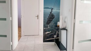A hallway with a door leading to a room, a black console table with a vase, and a mural of a cable car on a mountain backdrop. - #HV | Le Panorama 🏔️ (Saint-Martin-d'Hères)