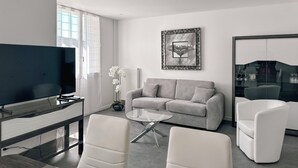 A modern living room with a grey sofa, white armchairs, a glass coffee table, and a flat-screen TV. - #HV | Le Panorama 🏔️ (Saint-Martin-d'Hères)
