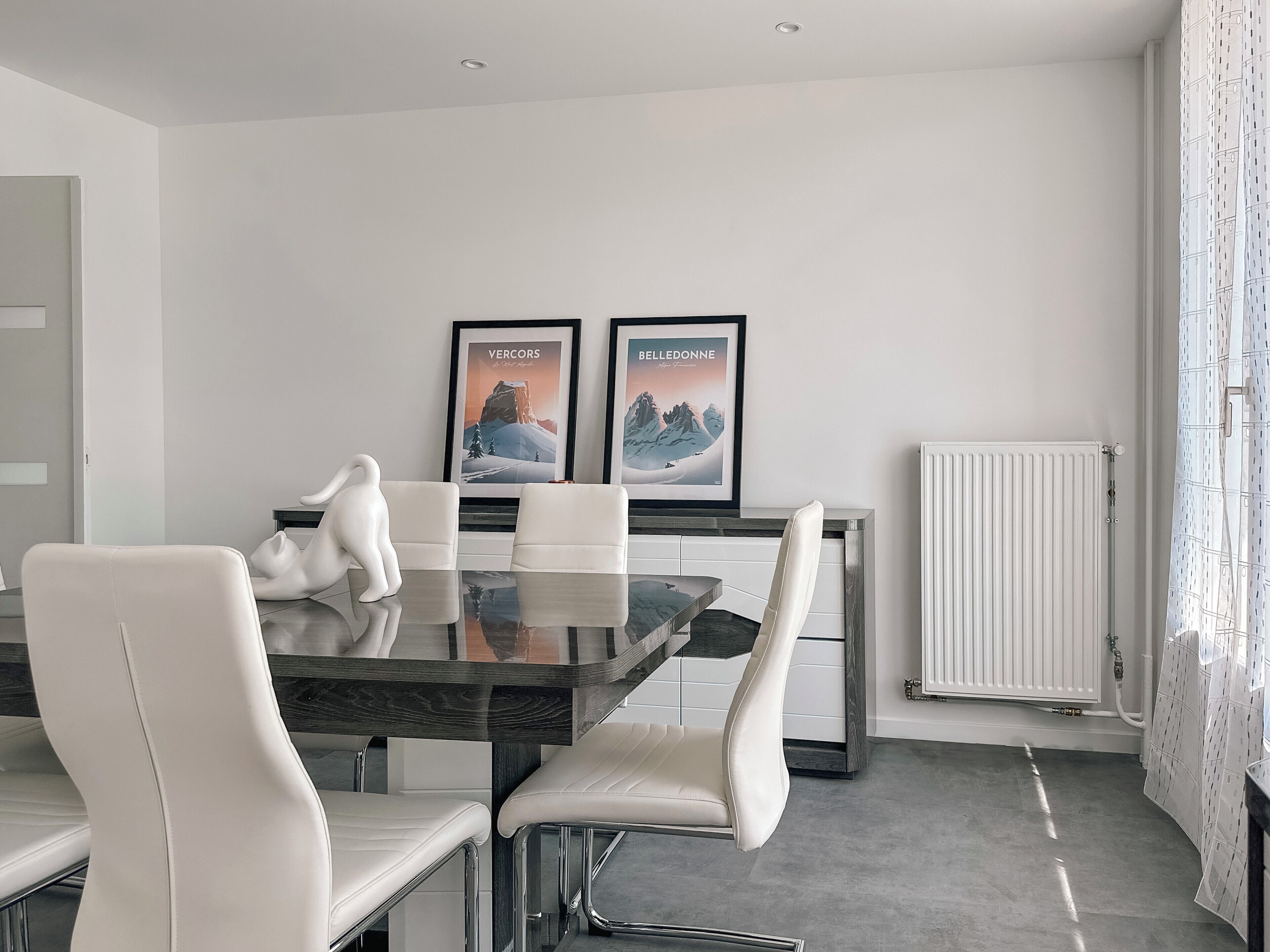 Un espace repas moderne avec une table en verre, des chaises blanches et deux tableaux encadrés accrochés au mur.