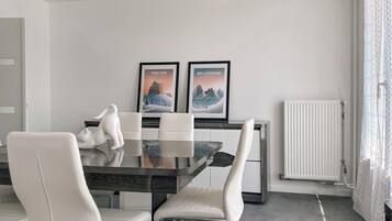 Un espace repas moderne avec une table en verre, des chaises blanches et deux tableaux encadrés accrochés au mur.