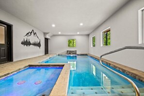 An indoor swimming pool with a mountain mural, a bench, and windows with greenery views. - Luxe 6BR Pool Cabin*Hot Tub*Arcade*Sleeps 20 (Sevierville)
