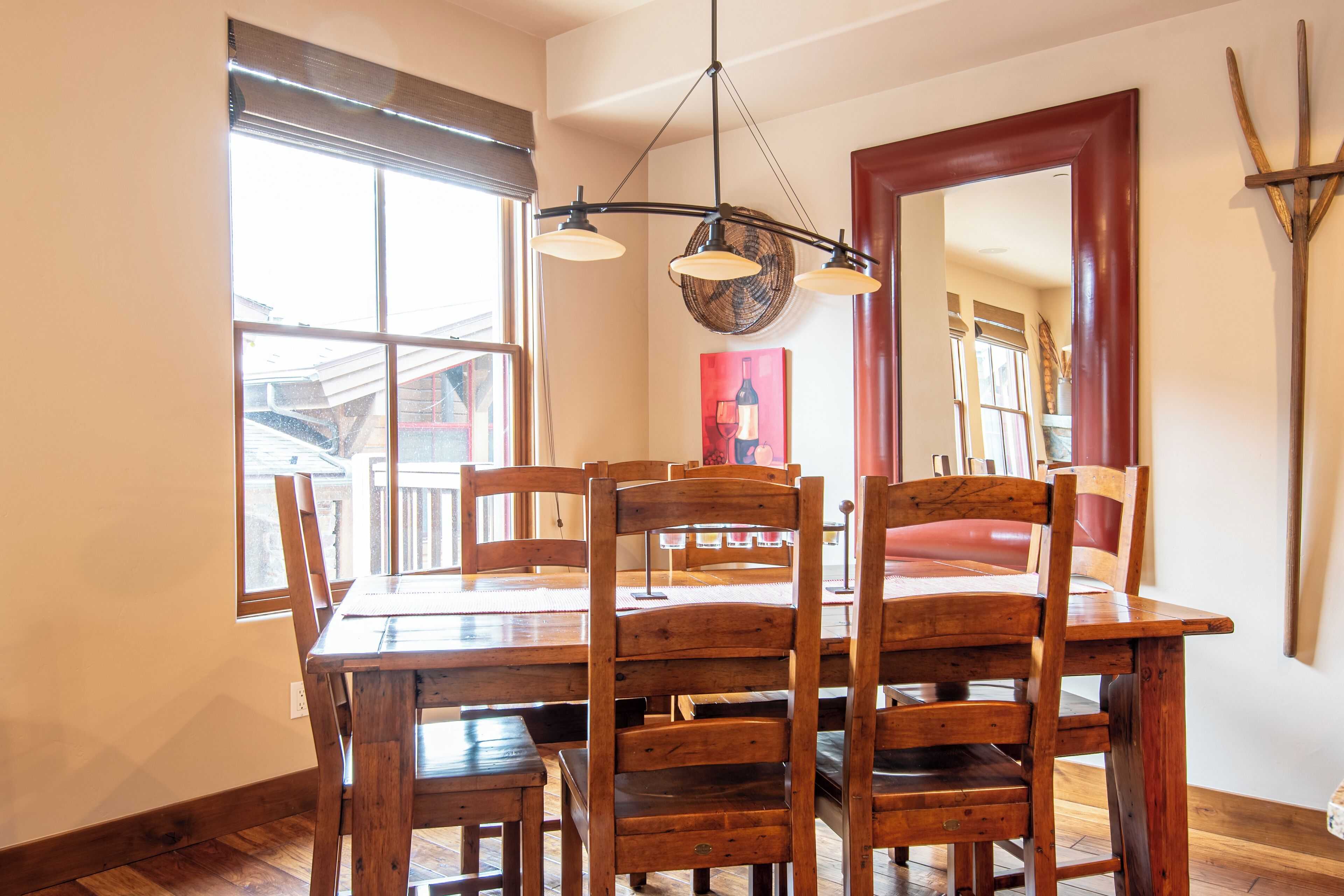 A dining area with a wooden table and chairs, a chandelier, and a large mirror on the wall.