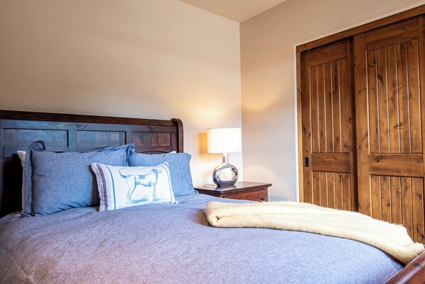 Una cama bien hecha con una almohada azul y blanca, una manta blanca y un cabecero de madera.