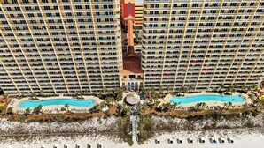 A high-rise hotel with multiple balconies, a central pool, and a beach area with sun loungers.