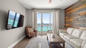 A living room with a TV, a leather sofa, a coffee table, and a view of the ocean through large sliding doors.