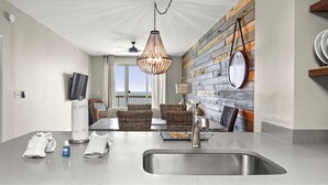 A modern kitchen with a large island, a hanging light fixture, and a view to the outside.