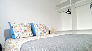 A neatly made bed with floral bedding and a grey throw blanket, a bedside table with a lamp, and a window with a white blind. - Single-storey 3-bedroom house with garden in the heart of La Gacilly (La Gacilly)