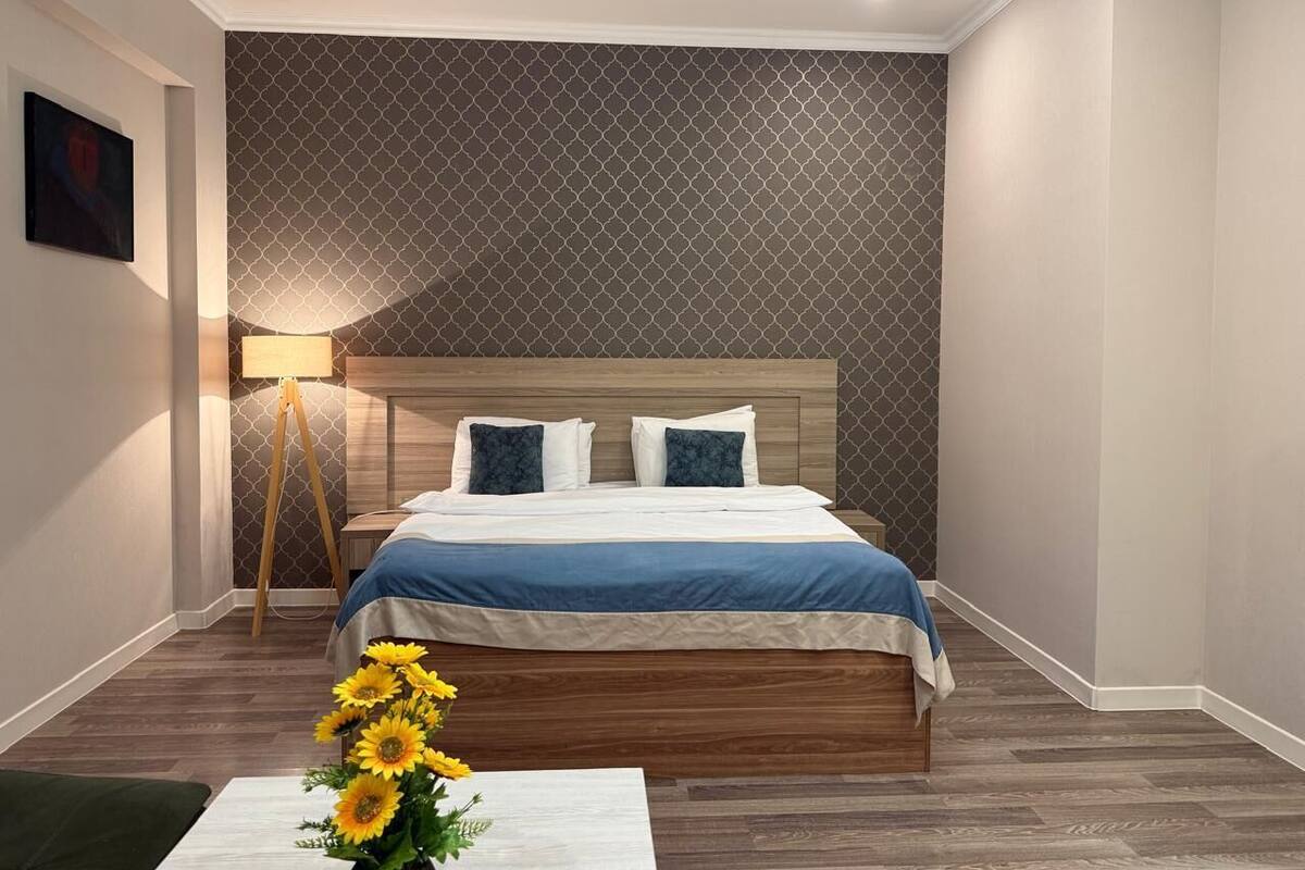 A neatly arranged bedroom with a wooden bed, a standing lamp, and a vase of sunflowers.
